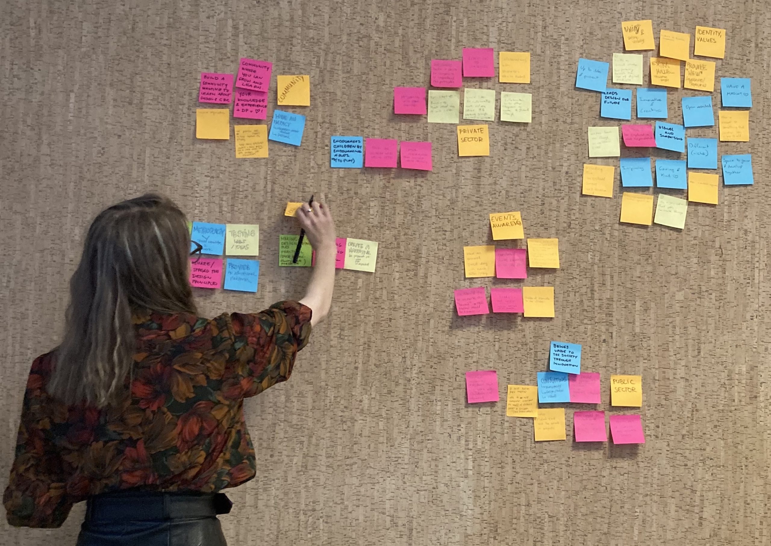 Young lady on the left adding colorful post-it notes on the wall during a workshop.